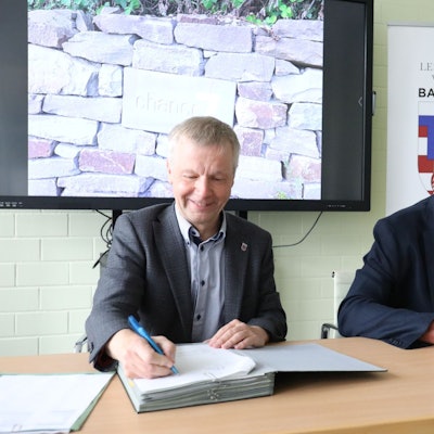 Zwei Männer sitzen nebeneinander an einem Tisch und unterschreiben die Verträge. Im Hintergrund das Stadtlogo mit dem Motto „Lebensfreude verbürgt“.