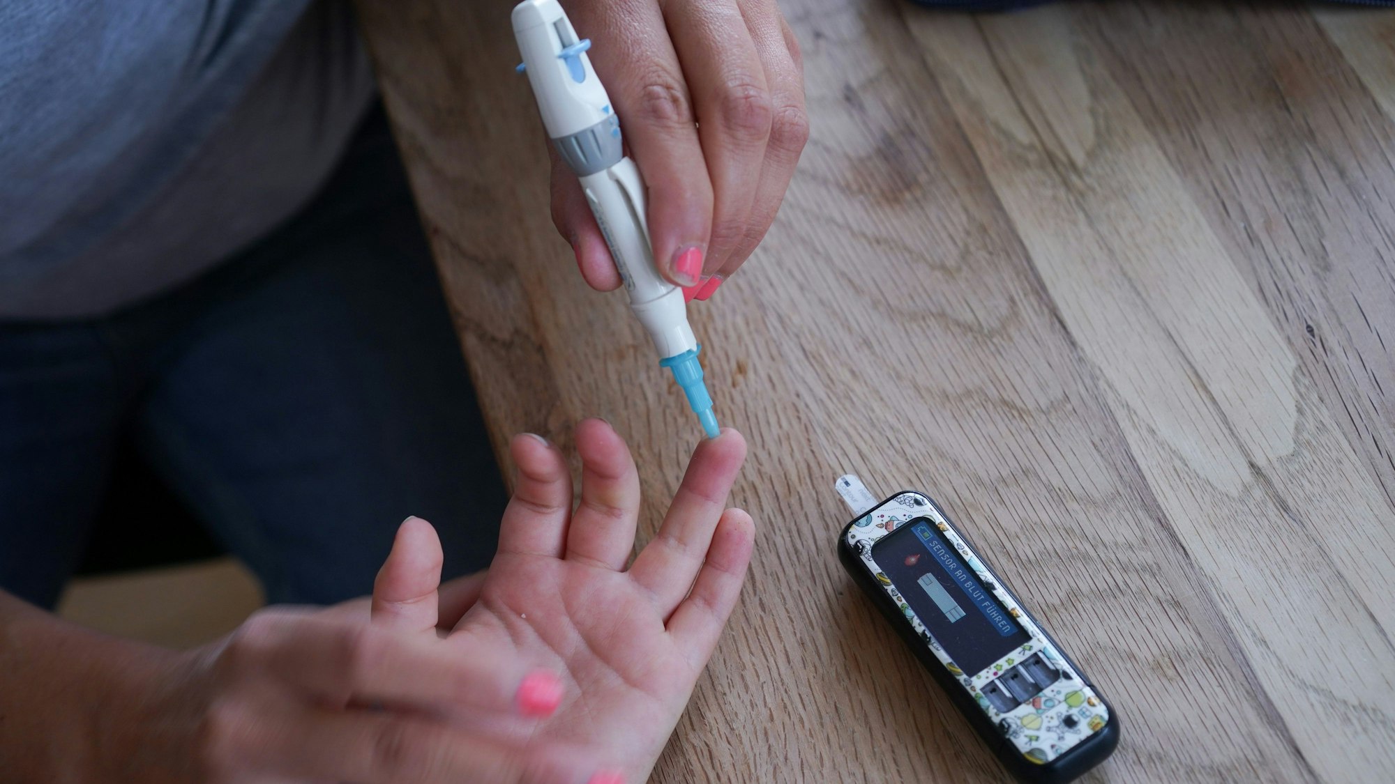 Das Bild zeigt eine Frau, die bei einem Kind einen Blutzuckertest macht.