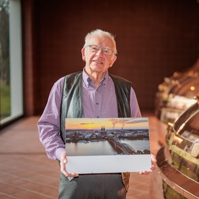 Ein älterer Mann hält ein Foto in den Händen, das den Kölner Dom, den Rhein und die Hohenzollernbrücke aus der Luftperspektive zeigt.