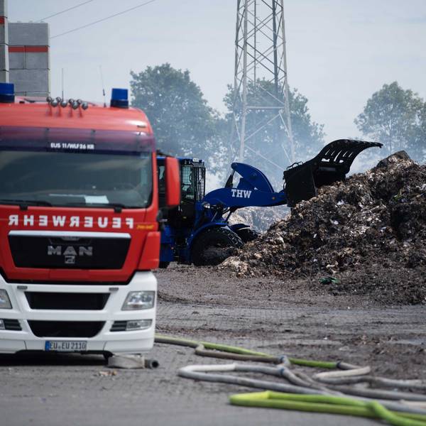 Ein Radler des THW zieht das abgelöschte Papier auseinander. Ein Feuerwehrfahrzeug ist im Vordergrund zu sehen.