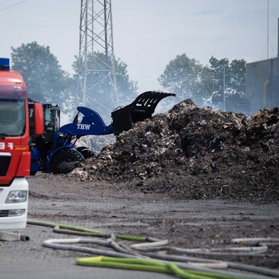 Ein Radler des THW zieht das abgelöschte Papier auseinander. Ein Feuerwehrfahrzeug ist im Vordergrund zu sehen.