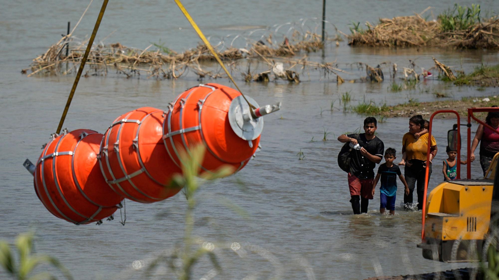Migranten beobachten die großen Bojen, die als Grenzsperre im Fluss Rio Grande eingesetzt werden sollen.