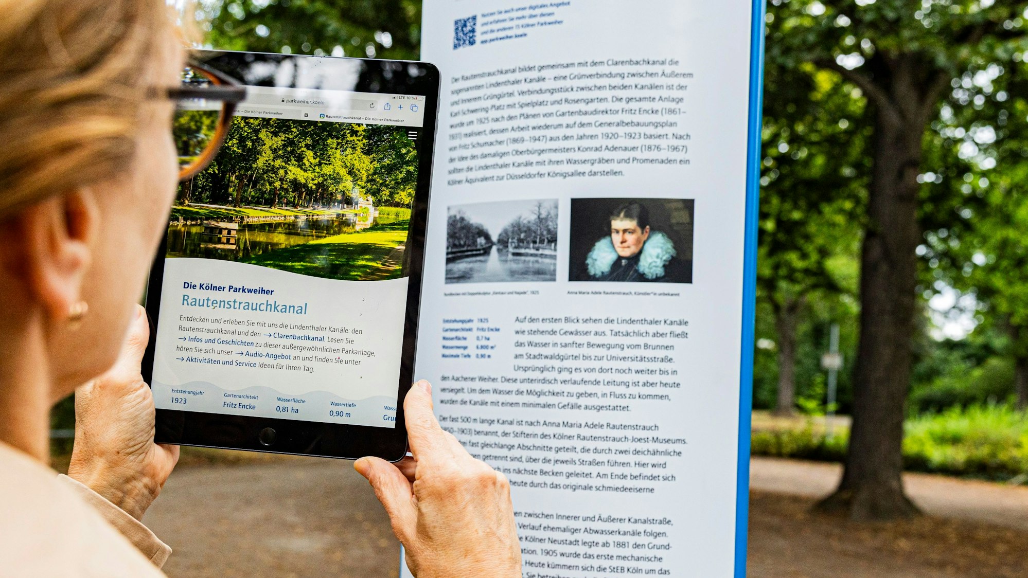 Eine Frau scannt mit einem Tablett einen QR-Code auf einer Infosäule am Rautenstrauchkanal.