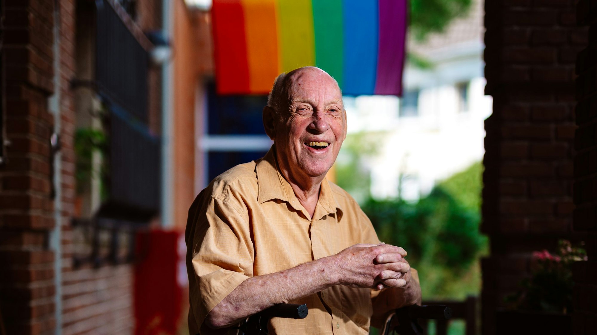 Ein alter Mann sitzt vor einer Regenbogenflagge.
