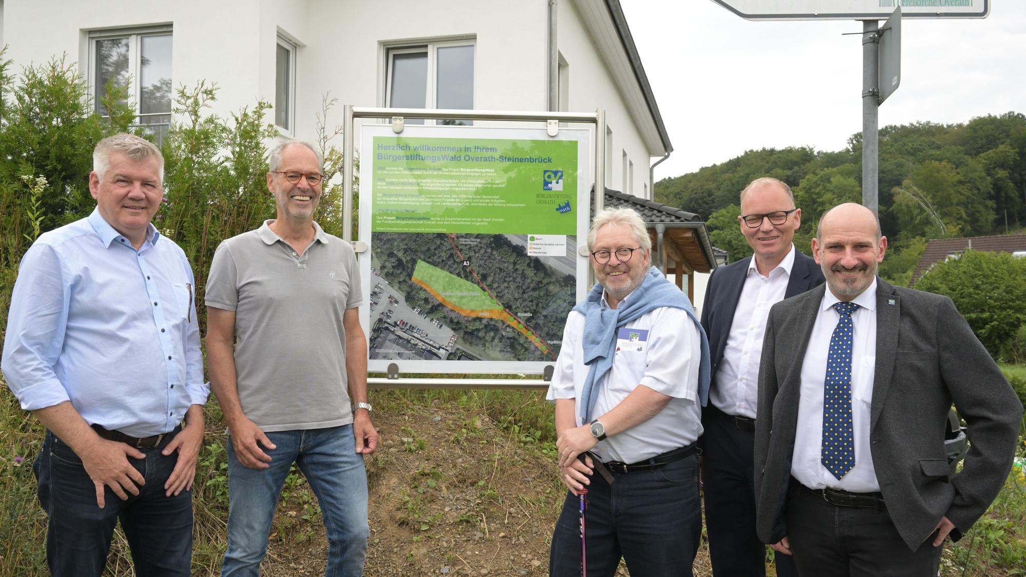 Fünf Männer stehen vor einer Schautafel, die den Bürgerwald in Steinenbrück erläutert.