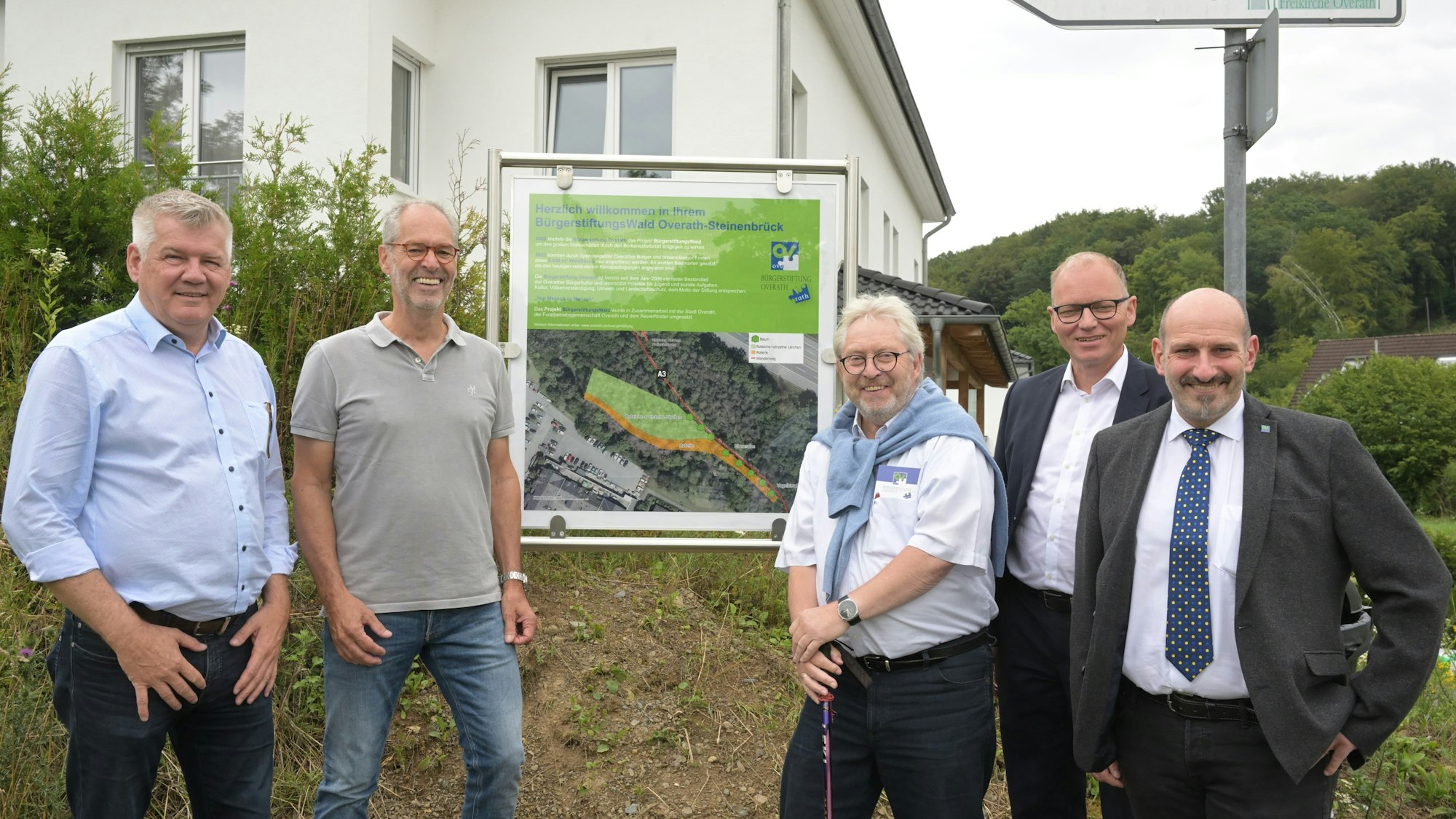 Fünf Männer stehen vor einer Schautafel, die den Bürgerwald in Steinenbrück erläutert.