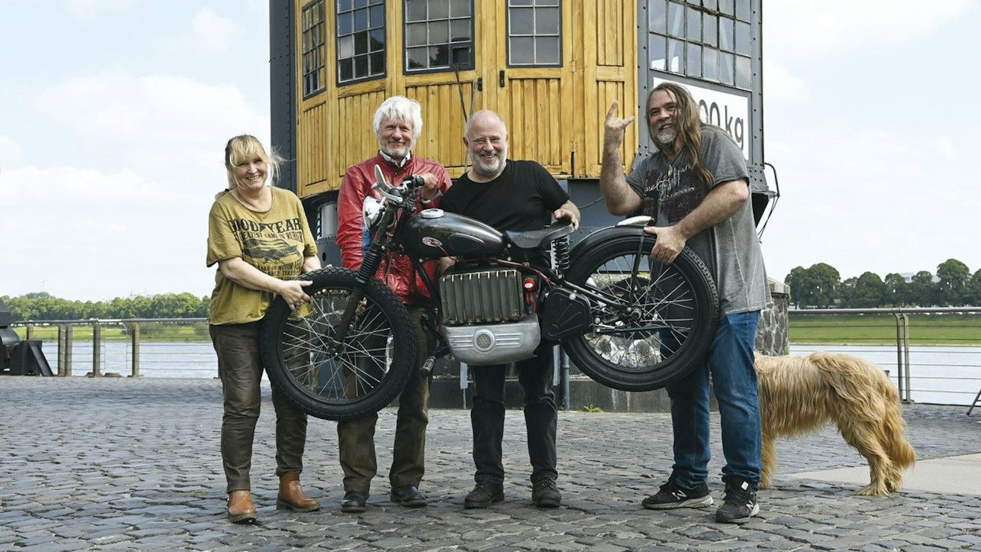 Vier Menschen stehen vor einem Kran am Rheinauhafen mit dem neu umgebauten Motorrad