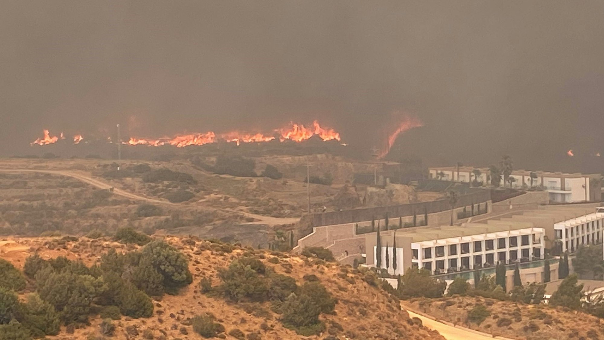 Auf dem Foto sind lodernde Flammen nahe einem Gebäude zu sehen, schwarzer Rauch breitet sich aus.