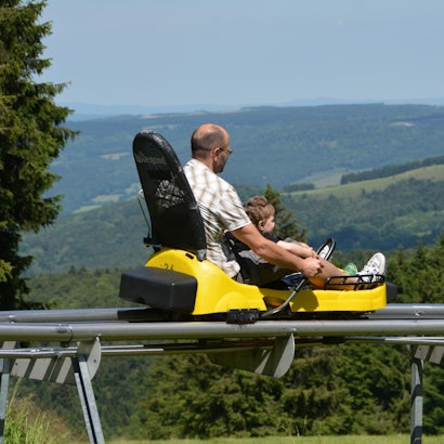Ein Mann fährt mit einem Kind zusammen in einem Sommerrodelschlitten.