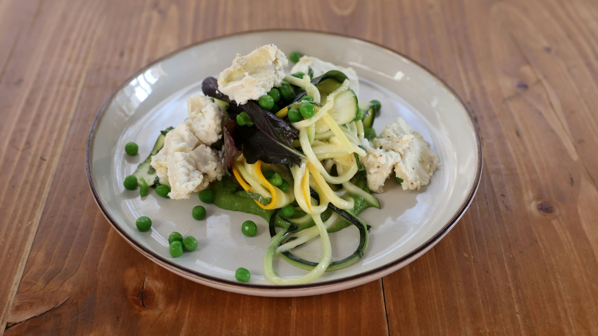 Zucchini-Nudeln, mit Erbsen und Ziegenkäse auf einem Teller angerichtet
