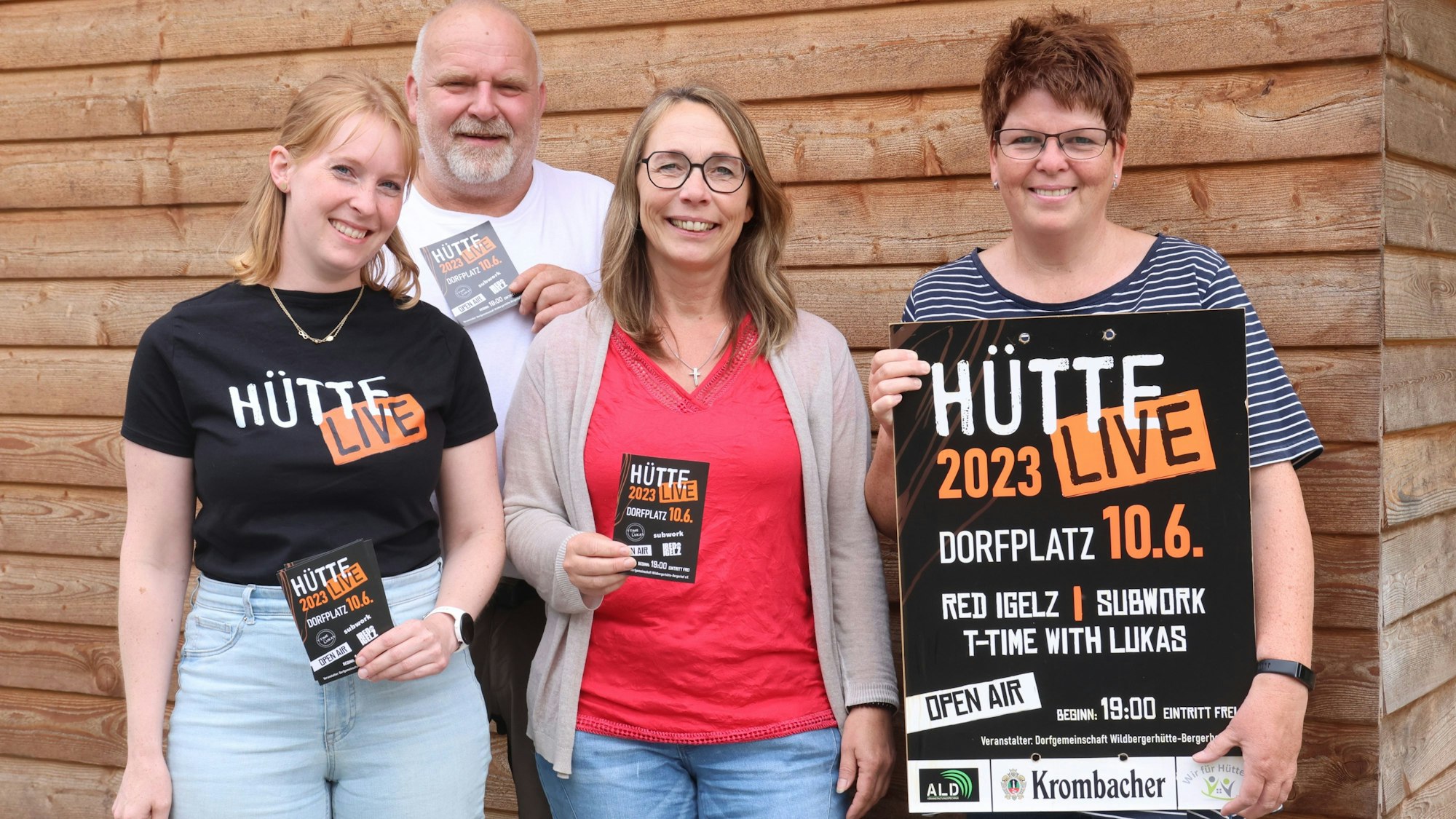 Drei Frauen und ein Man stehen zusammen. Sie halten Flyer und ein Plakat des Open Airs „Hütte Live“ in den Händen.