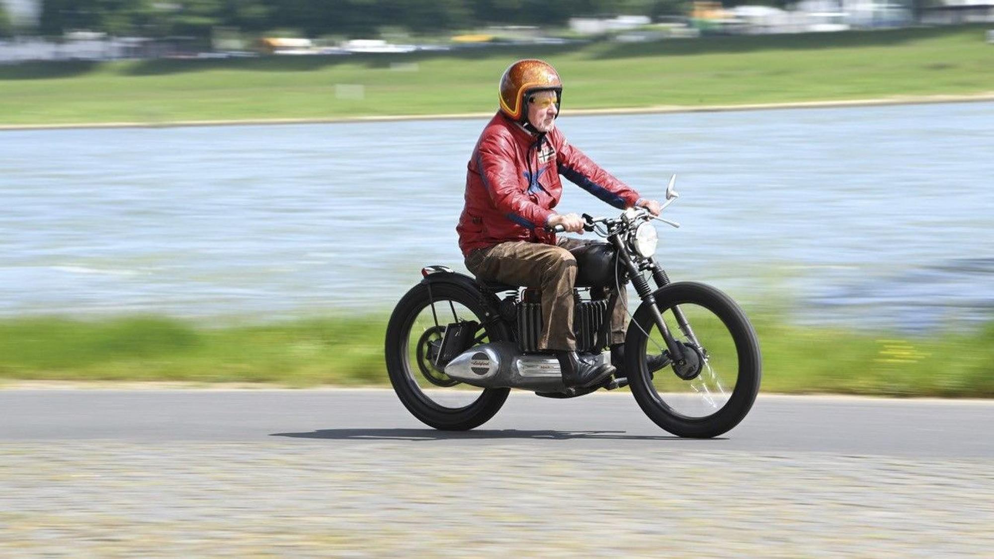 Jürgen Becker fährt auf dem E-Motorrad am Rhein entlang.