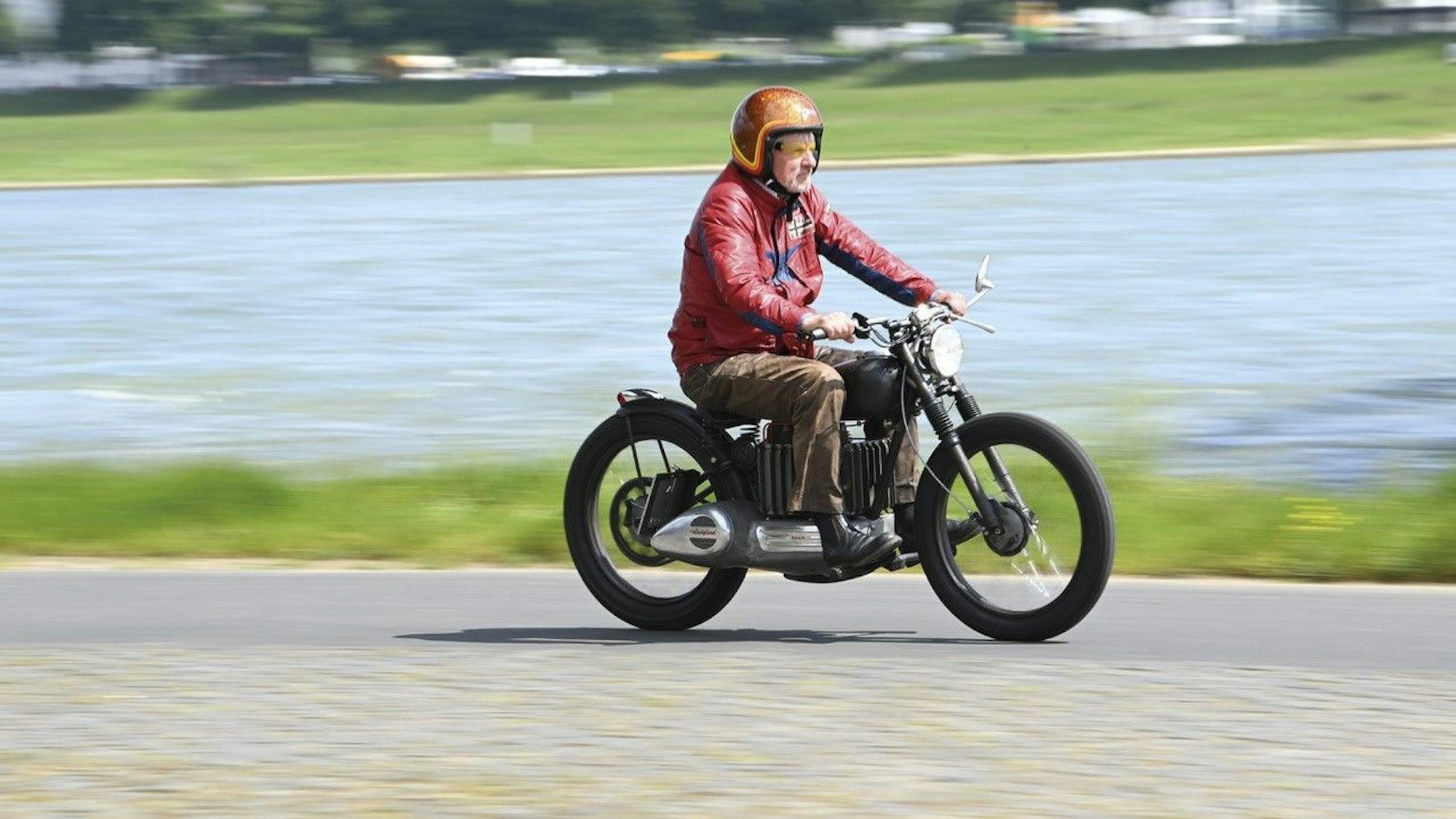 Jürgen Becker fährt auf dem E-Motorrad am Rhein entlang.