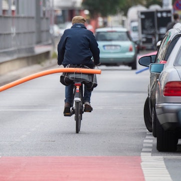Ein Fahrradfahrer hat eine Schwimmnudel auf seinen Gepäckträger geklemmt. Damit will er auf den nötigen Sicherheitsabstand im Straßenverkehr hinweisen.