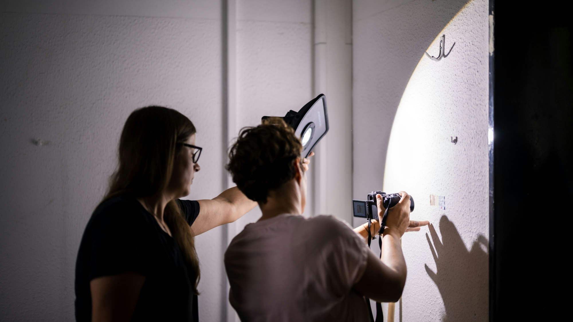 Zwei Frauen begutachten eine Wand und machen ein Foto.