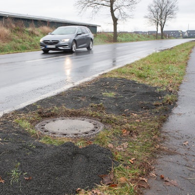 Niederkassel: Neben einer Landstrasse in Niederkassel-Lülsdorf sieht man den Kanaldeckel, wo ein Passant eine kopfüber steckende Leiche in einem Kanalschacht entdeckt hat.