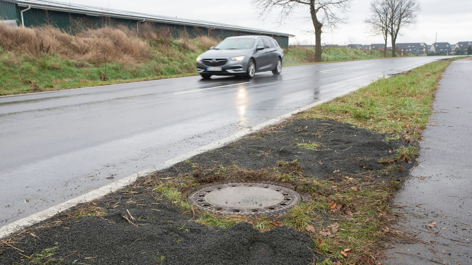 Niederkassel: Neben einer Landstrasse in Niederkassel-Lülsdorf sieht man den Kanaldeckel, wo ein Passant eine kopfüber steckende Leiche in einem Kanalschacht entdeckt hat.