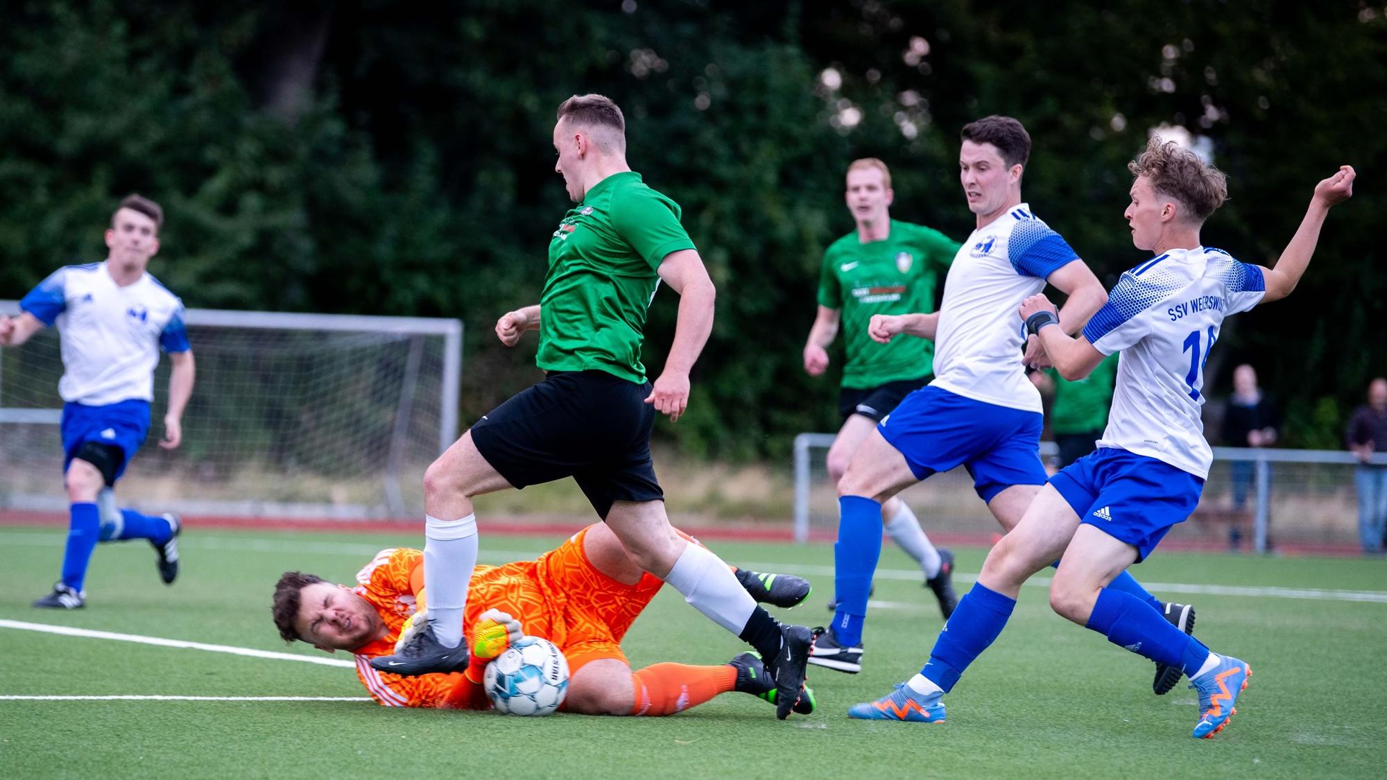 Weilerswists Torwart liegt am Boden und greift mit geschlossenen Augen nach dem Ball, bedrängt von einem Stürmer der Flamersheimer.