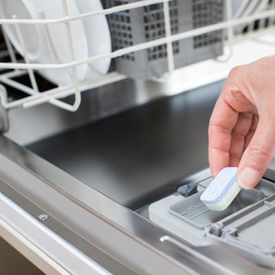 Nahaufnahme einer Person, die einen Spülmaschinentab in das entsprechende Fach einer Spülmaschine gibt.