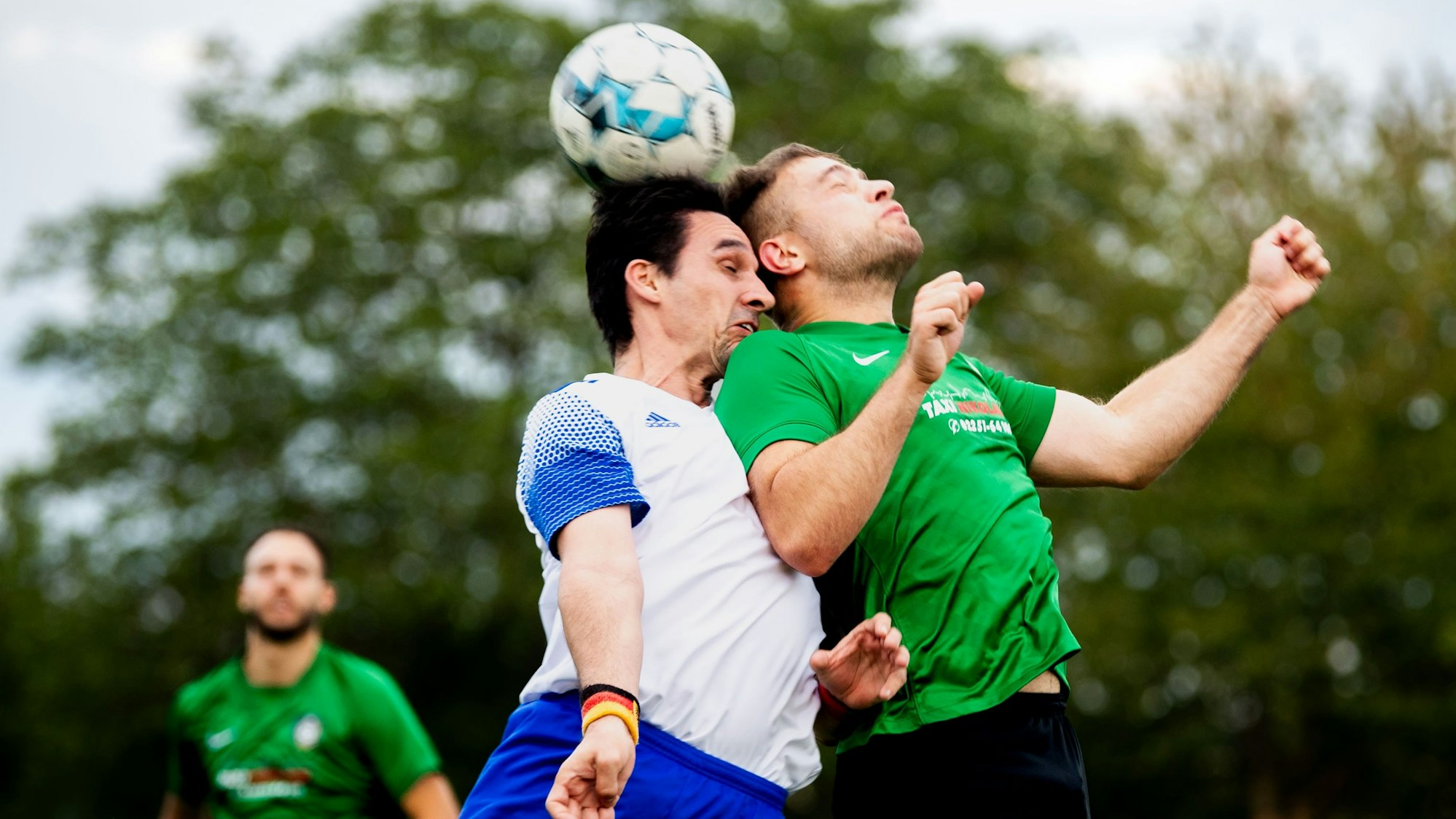 Zwei Fußballspieler springen hoch und köpfen mit geschlossenen Augen den Ball.
