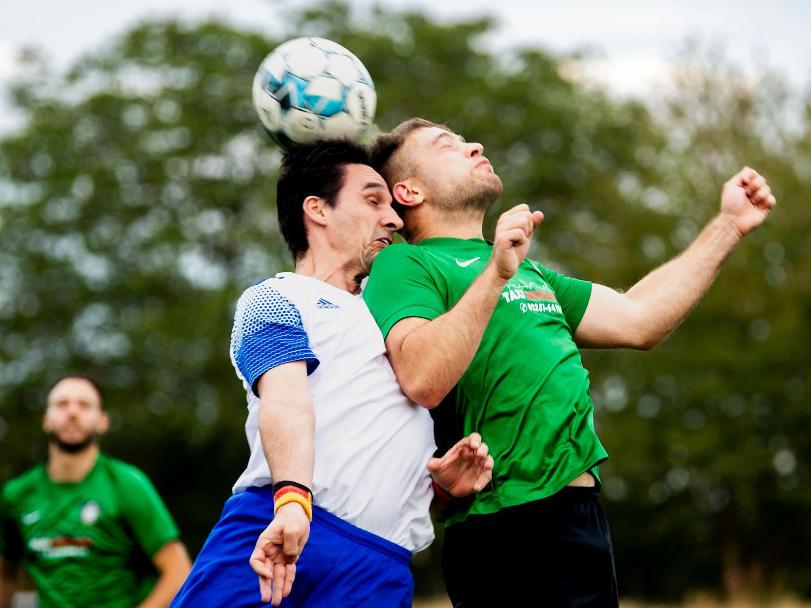 Mit geschlossenen Augen steigen zwei Fußballer zum Kopfballduell hoch.