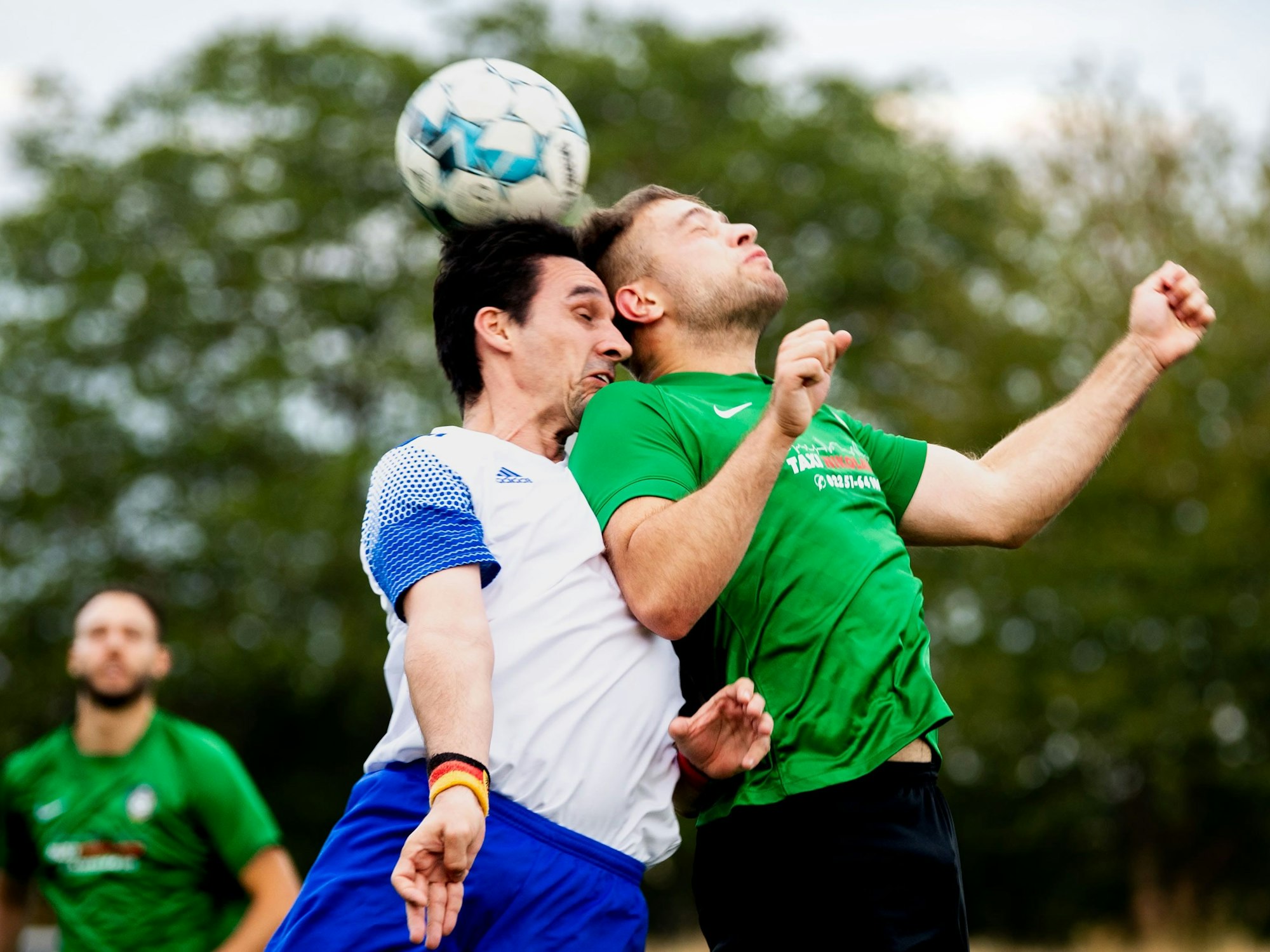Mit geschlossenen Augen steigen zwei Fußballer zum Kopfballduell hoch.