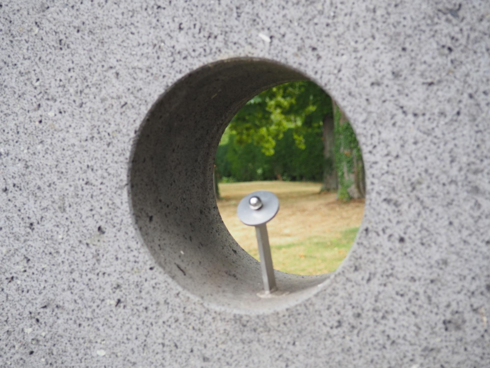 Ein Metallstab mit einer aufgesetzten kleinen Kugel ist Teil einer Betonskulptur.