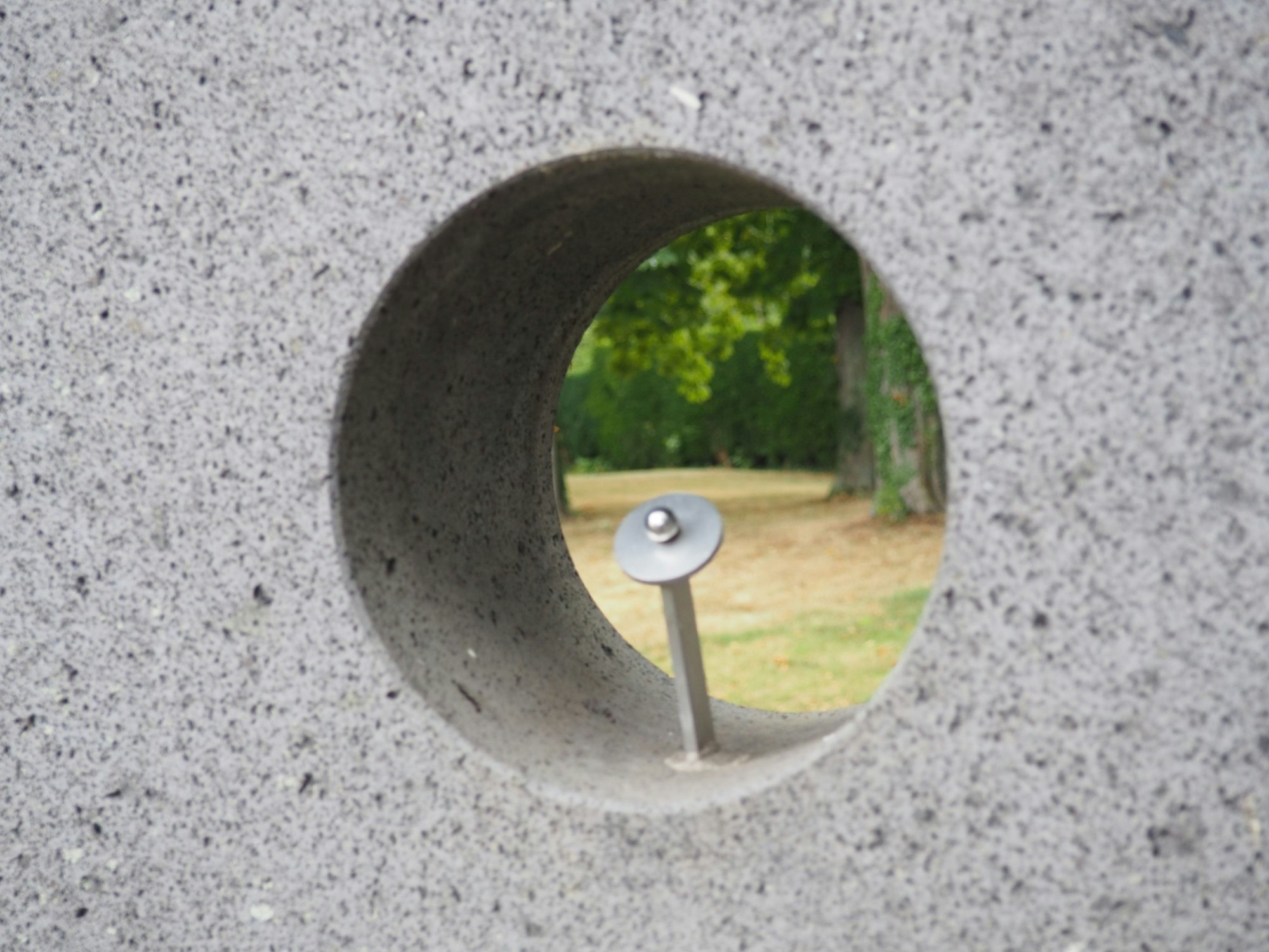 Ein Metallstab mit einer aufgesetzten kleinen Kugel ist Teil einer Betonskulptur.