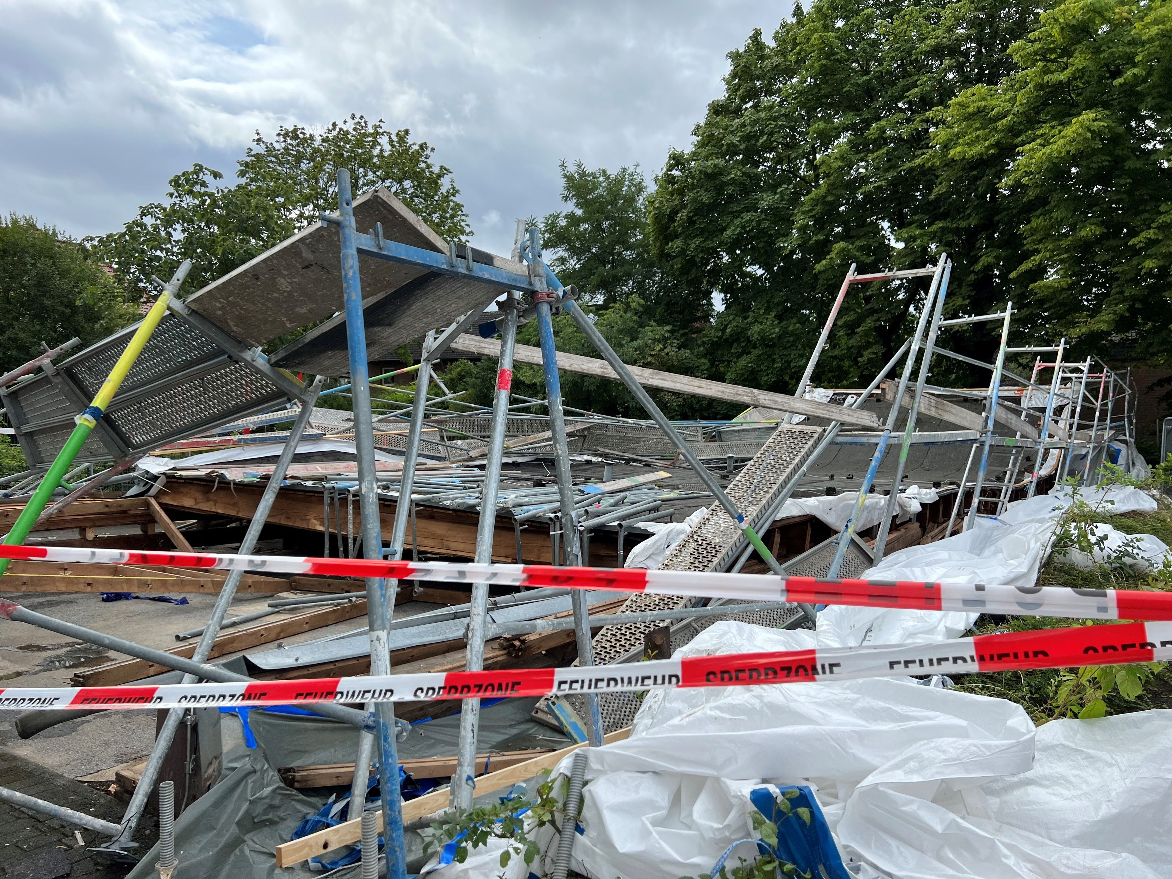 Hinter einem rot-weißen Absperrband der Polizei sind nur Trümmer des Baugerüsts und Holzteile zu sehen, die übereinander liegen.