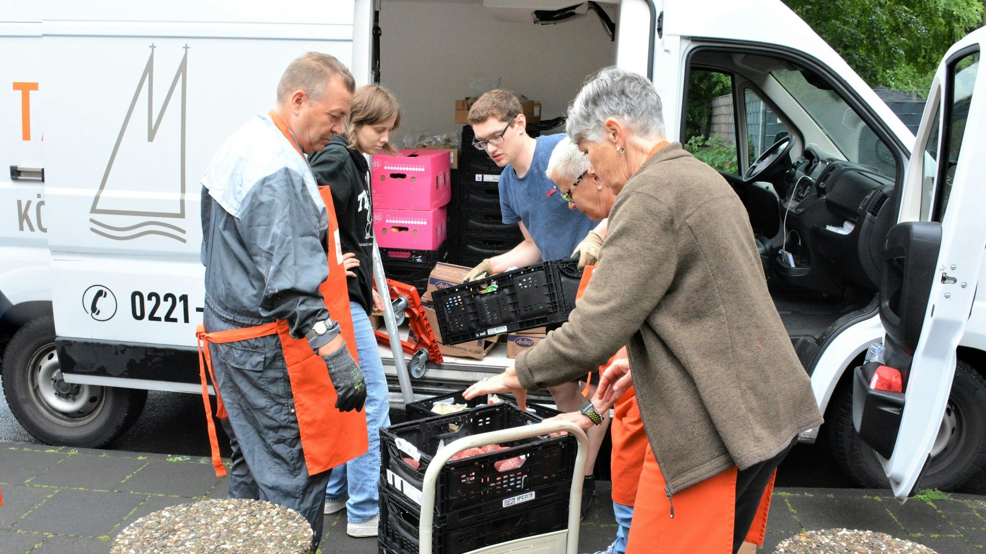 Menschen laden Klappkisten mit Lebensmitteln aus einem Lieferwagen auf eine Transport-Karre.