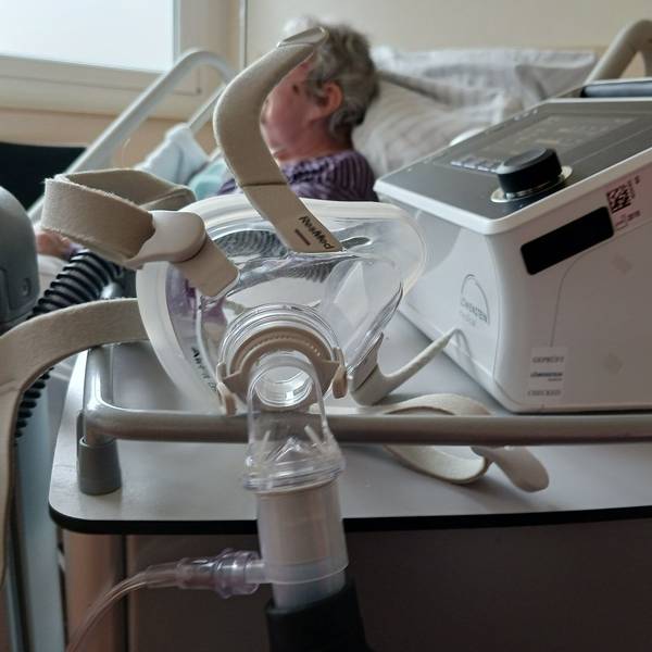 Eine Seniorin liegt in einem Krankenhausbett, im Vordergrund hängt eine Atemmaske am Beatmungsgerät. (Symbolfoto)