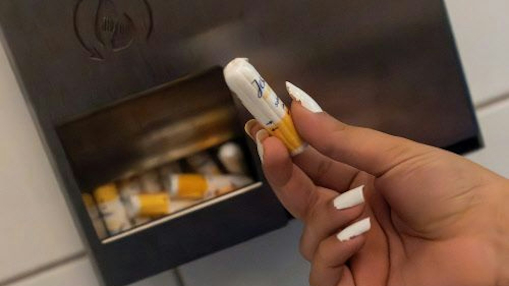 Eine Schülerin hält einen Menstruationsartikel vor einem Menstruationsartikel-Spender.