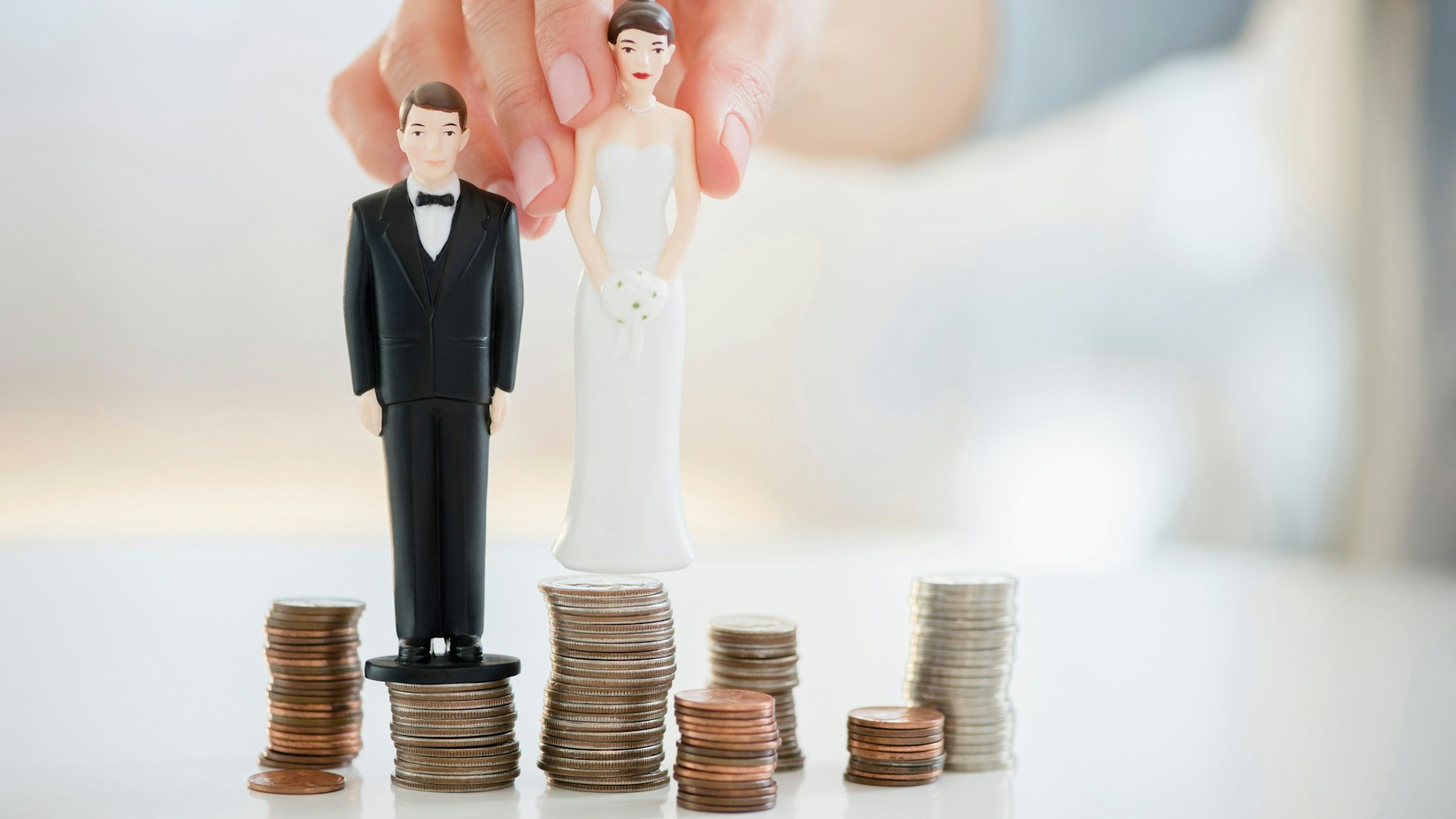 Nahaufnahme von Hochzeitstortenfiguren auf Münzstapeln.