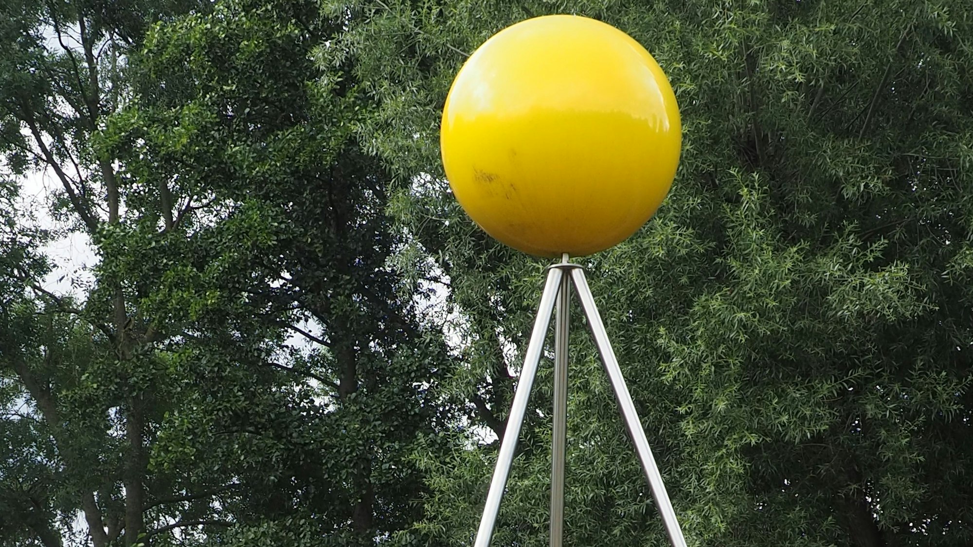 Eine gelbe Kugel, die die Sonne darstellt, liegt auf einem Metallgestell mit drei Beinen.
