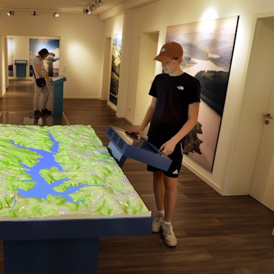 Menschen stehen an Stationen und einem großen Relief der interaktiven Ausstellung „Wasser verbindet“ im Auqalon-Forum an der Großen Dhünn-Talsperre.