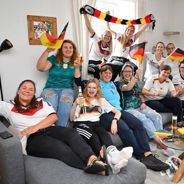 Die Frauen des TUS Marialinden sitzen auf der Couch und schwenken Fahnen.