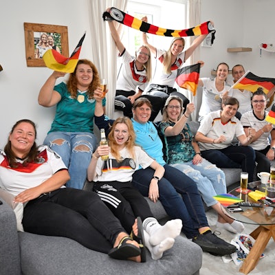 Die Frauen des TUS Marialinden sitzen auf der Couch und schwenken Fahnen.