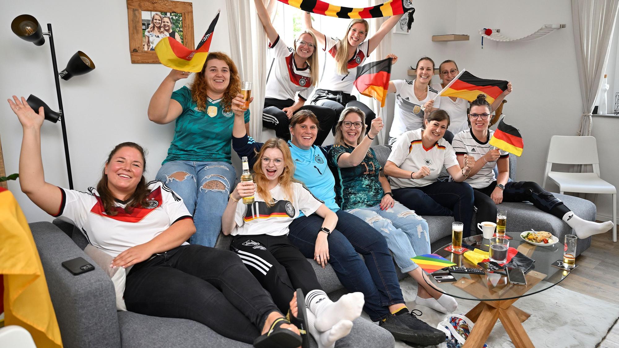 Die Frauen des TUS Marialinden sitzen auf der Couch und schwenken Fahnen.