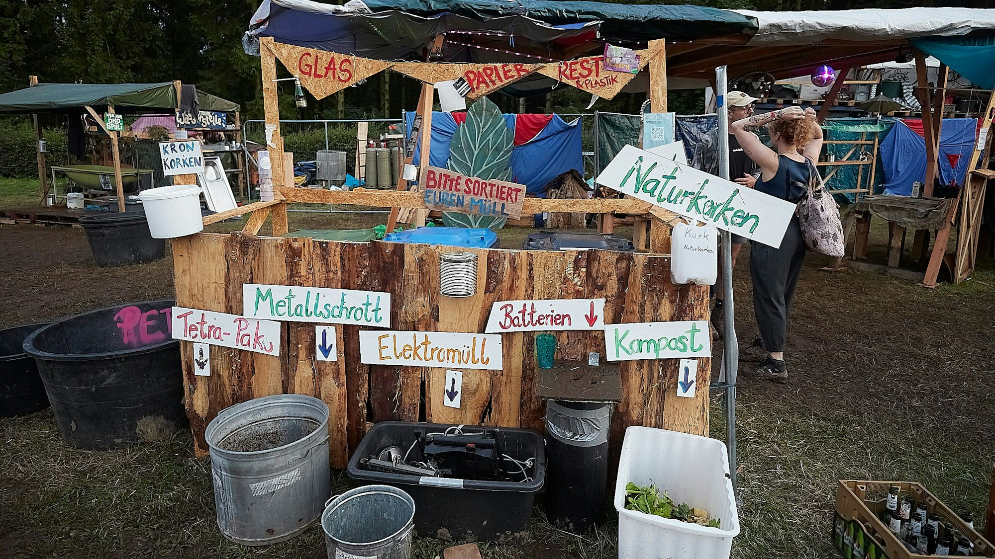 Das Bild zeigt eine aus Holz gestaltete Mülltrennungsstation bei einem Festival.