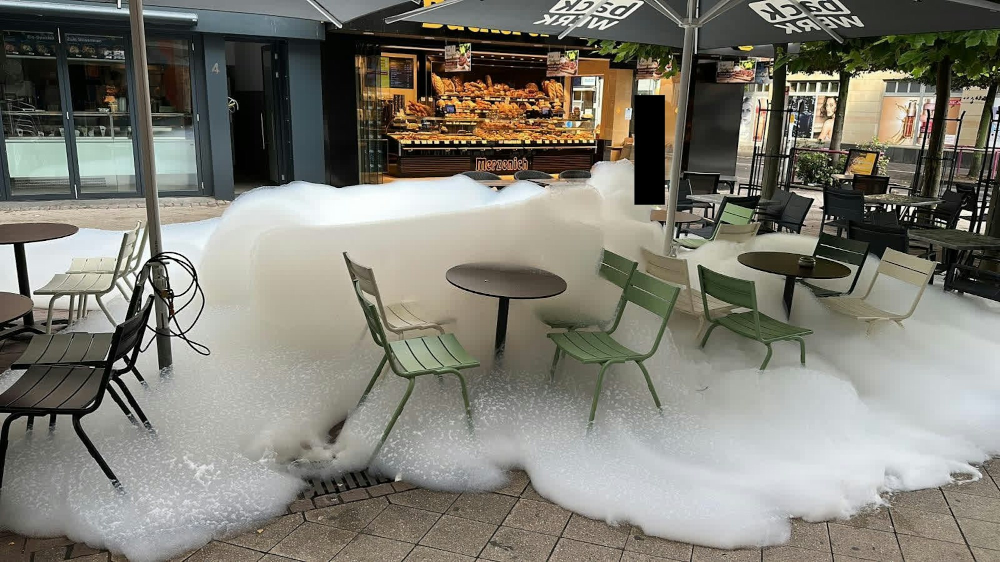 Mit weißem Schaum sind auch Tische und Stühle bedeckt, die im Außenbereich einer Bäckerei stehen.