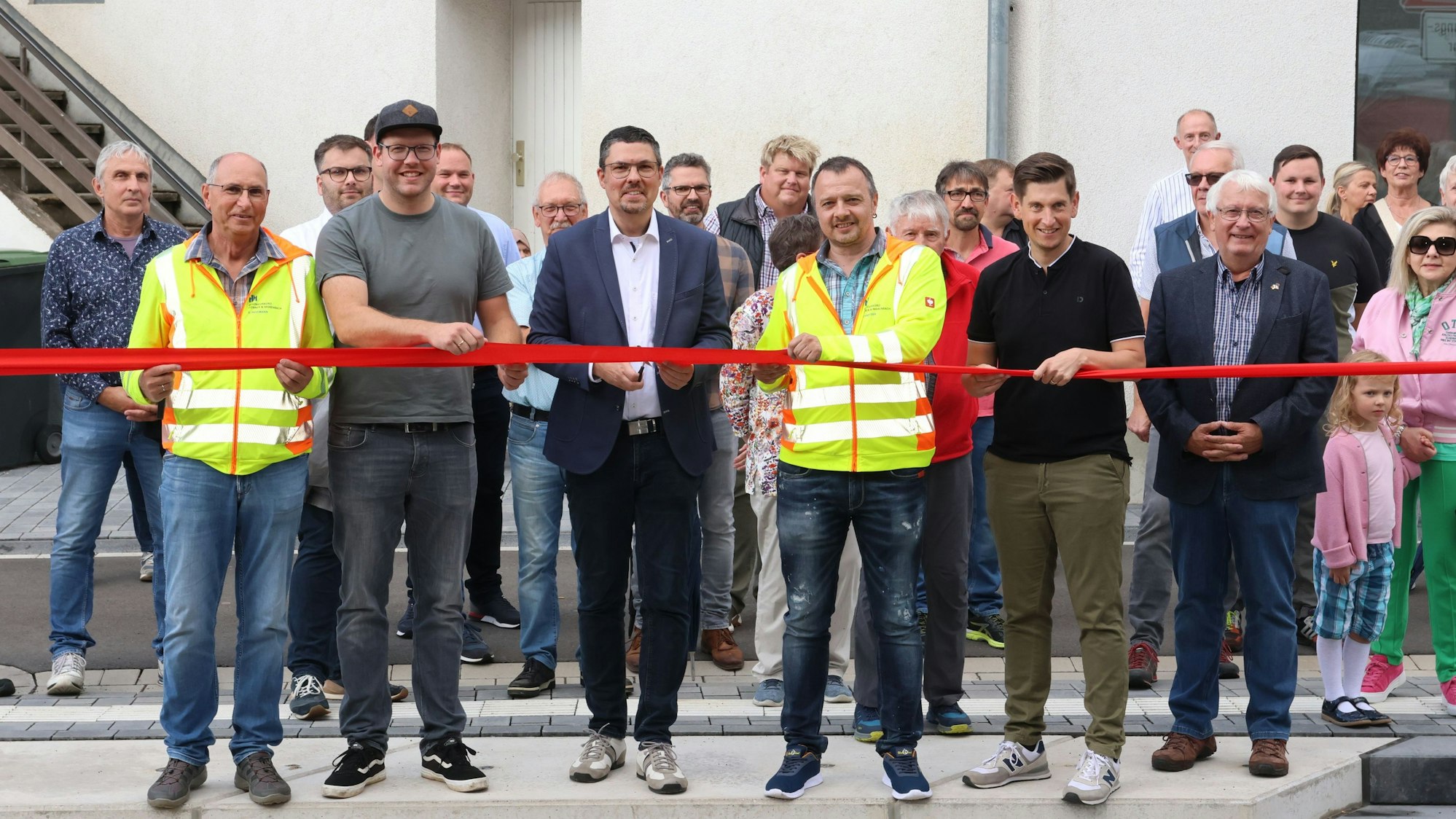 Zu sehen sind mehrere Menschen, die ein rotes band durchschneiden.