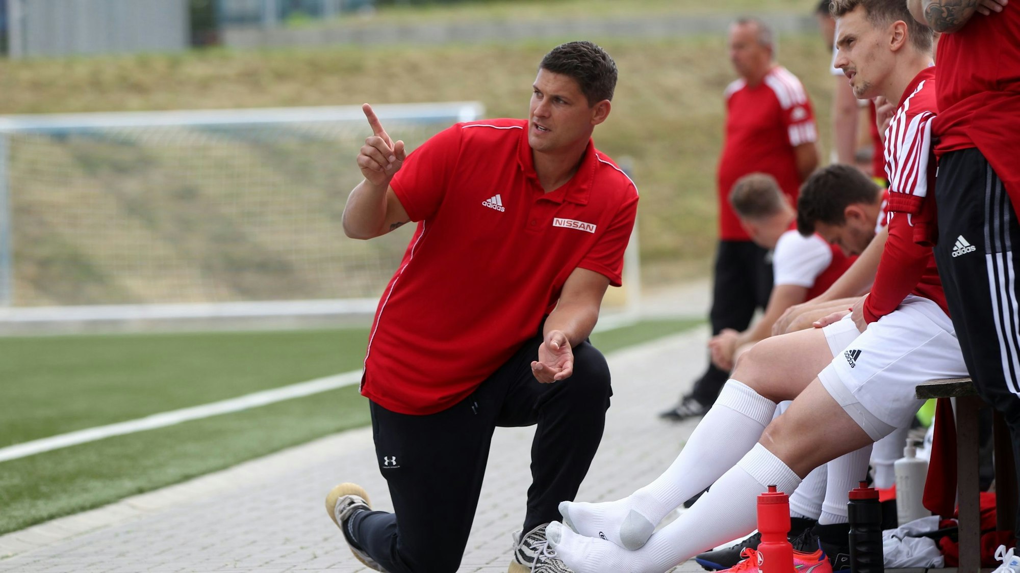 David Sasse kniet vor der Trainerbank und spricht mit einem Spieler.