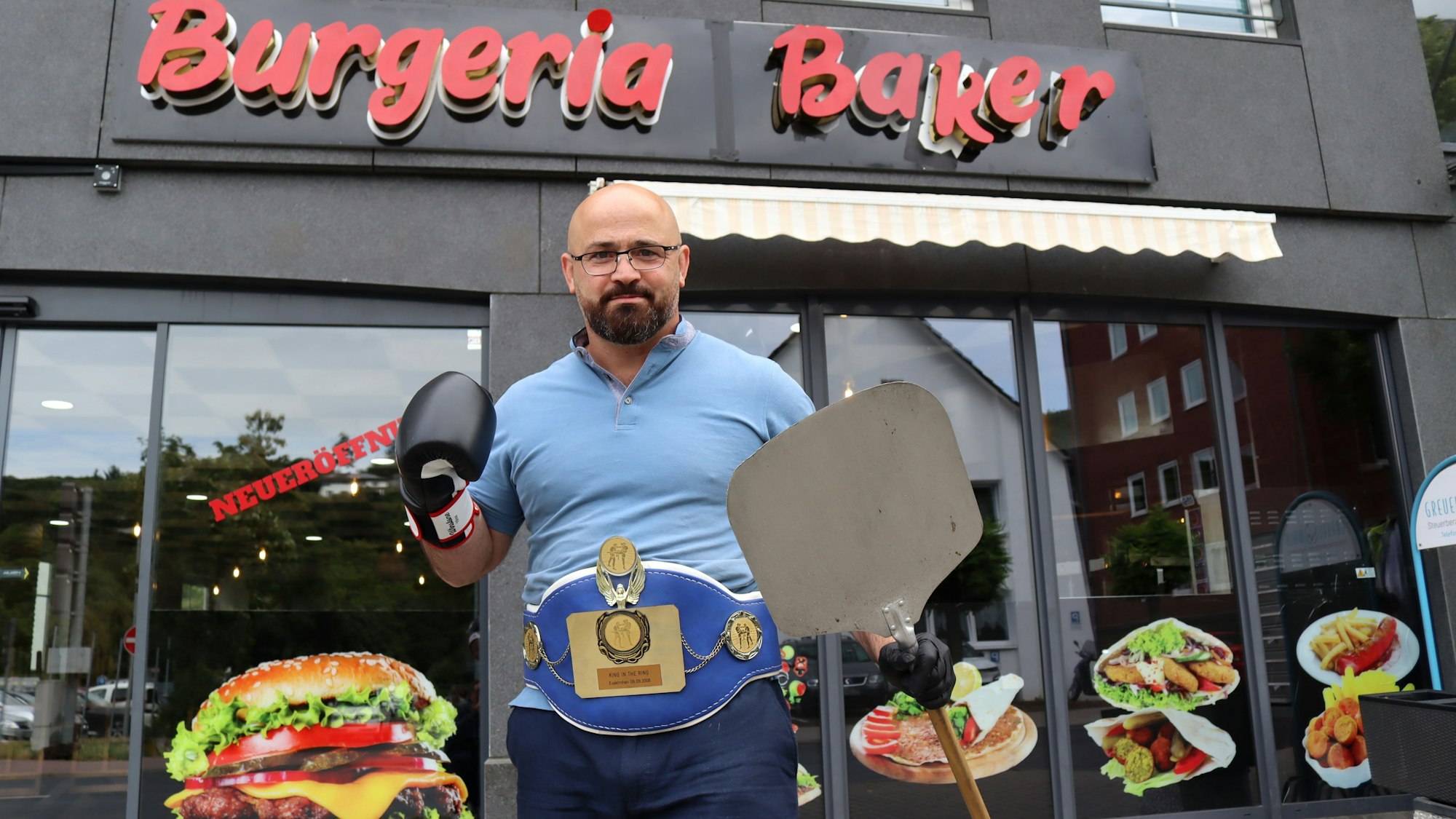 Baker Barakat vor seinem Schnellrestaurant: Rechts trägt er einen Boxhandschuh, in der linken Hand einen Pizza-Schieber.