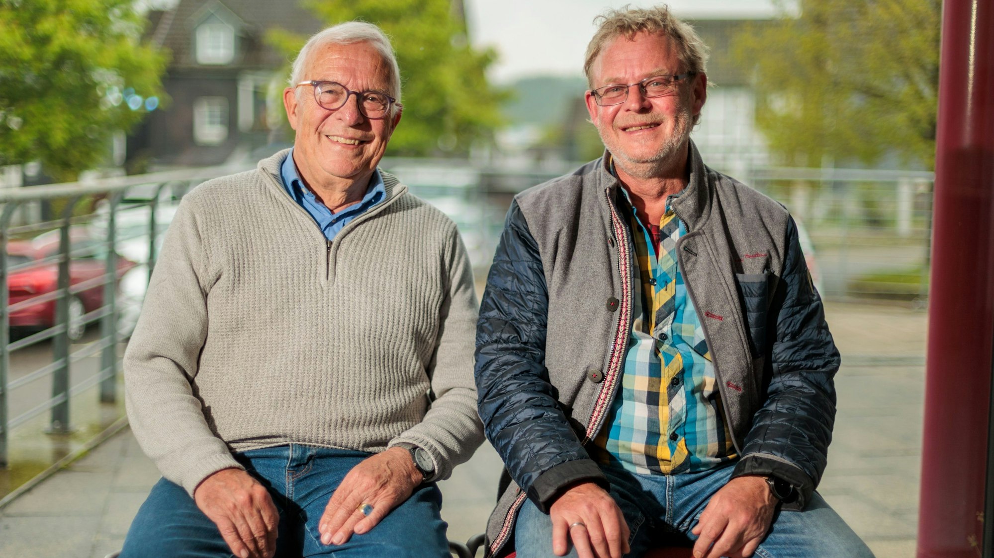 Zwei Männer sitzen nebeneinander und lächeln in die Kamera.