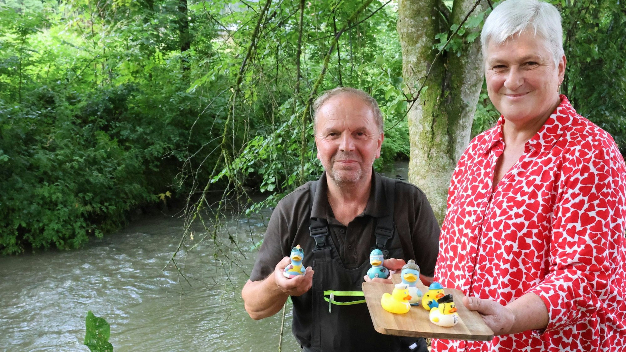 Ursula Savariello und ihr Ehemann Luigi mit Plastikenten stehen in Engelskirchen am Ufer der Leppe. in den Händen halten sie Plastikenten, die dort bei kultigen Rennen zu Wasser gelassen werden.
