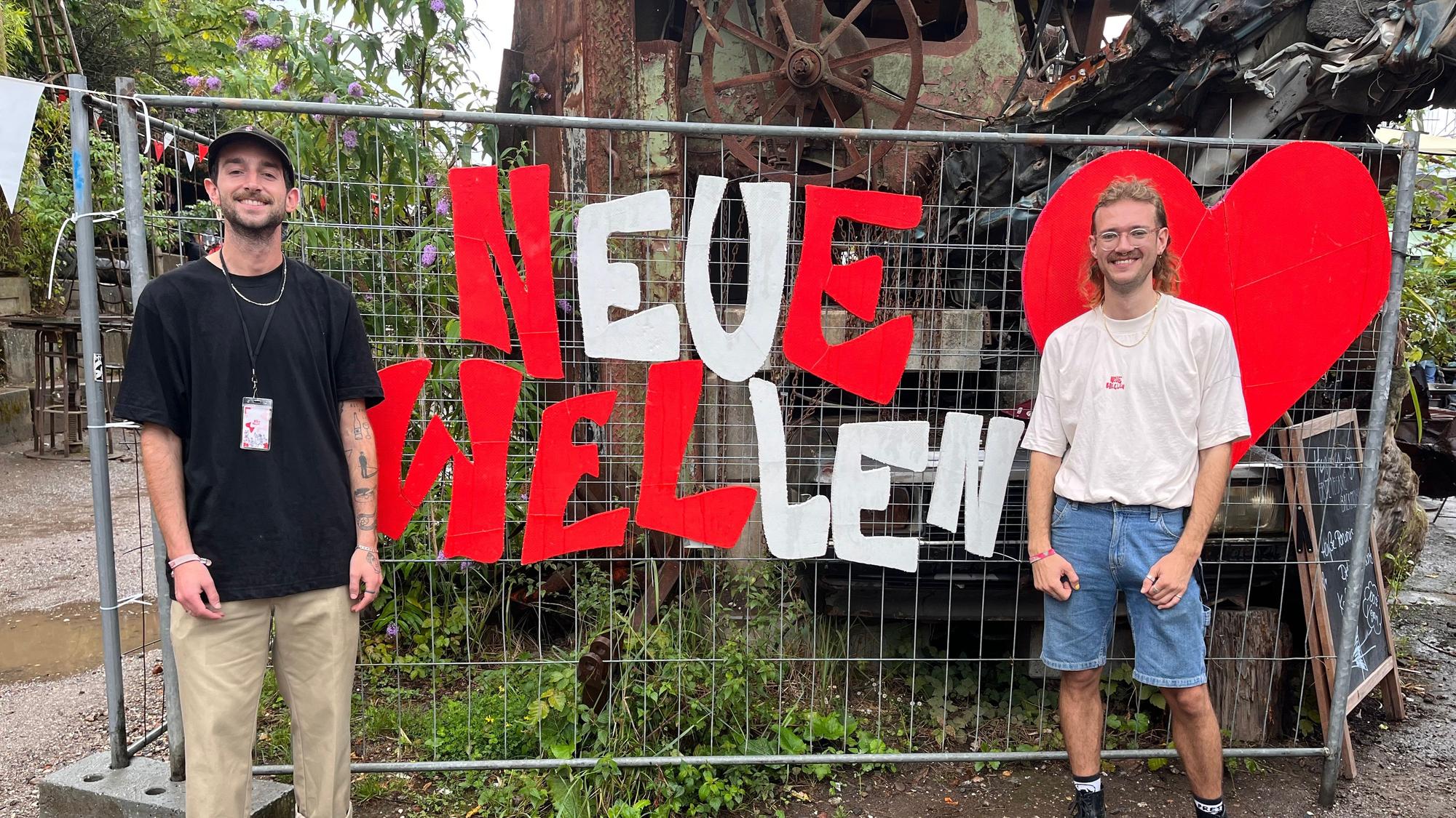 Die beiden Organisatoren stehen vor einem Bauzaun.