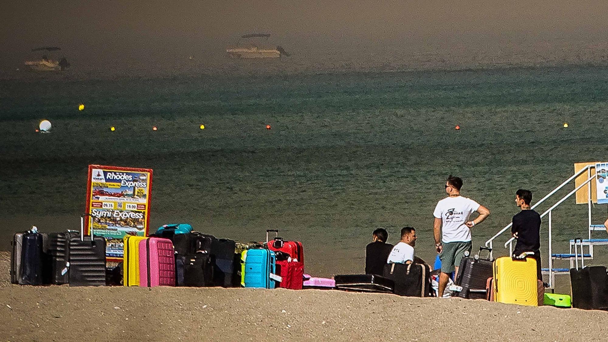 Menschen warten neben ihren Gepäckstücken am Strand, auf der griechischen Insel Rhodos, darauf, evakuiert zu werden.