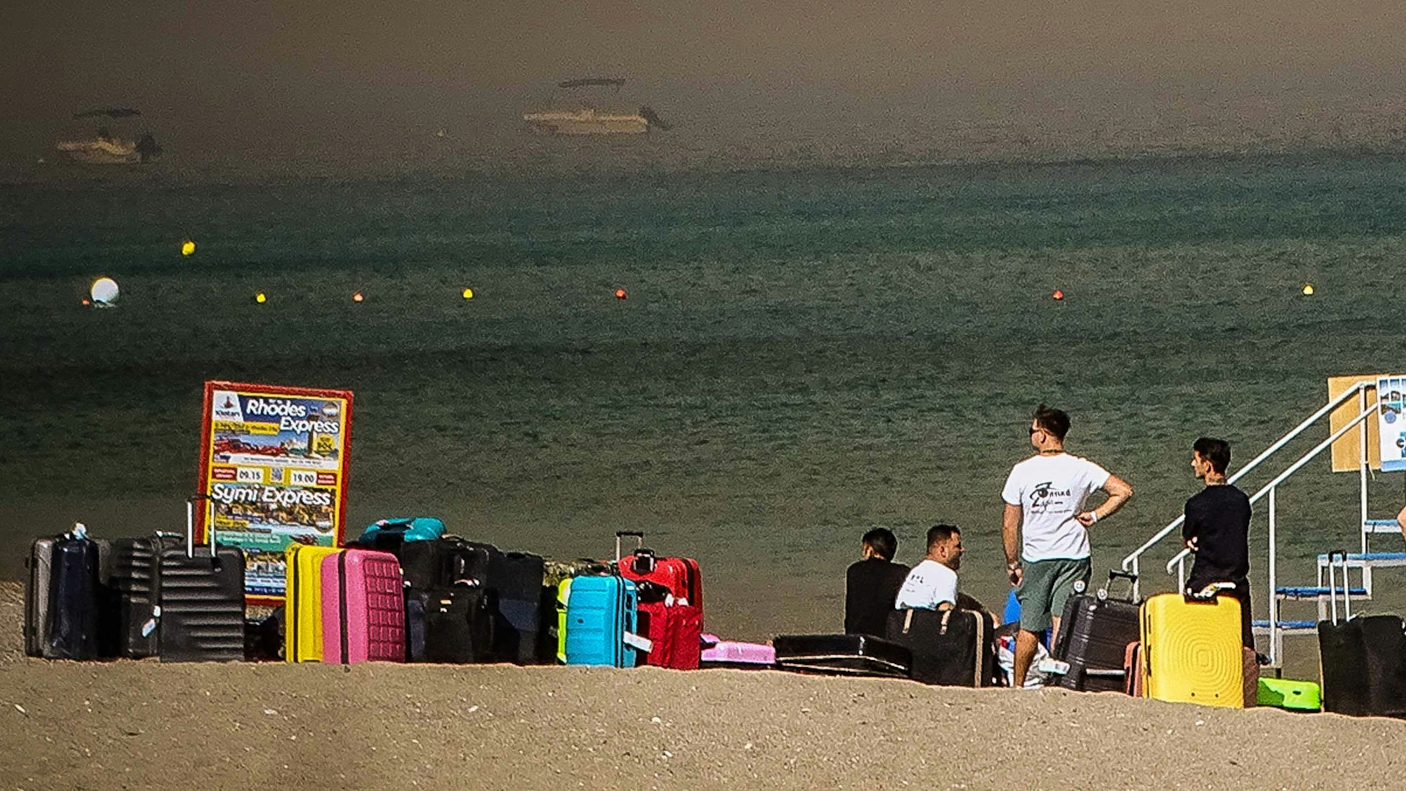 Menschen warten neben ihren Gepäckstücken am Strand, auf der griechischen Insel Rhodos, darauf, evakuiert zu werden.