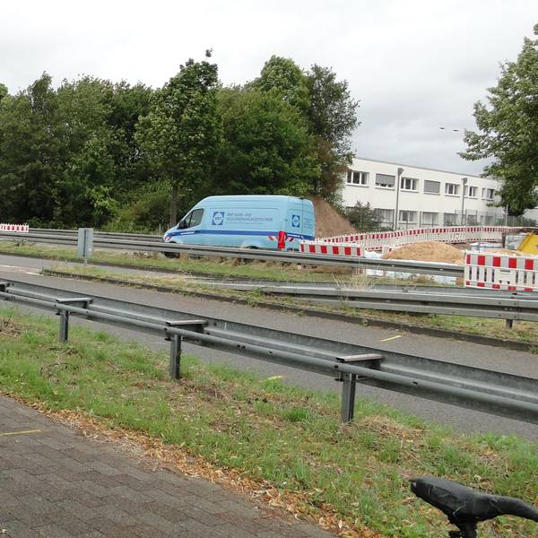 Autos fahren über eine Landstraße, ein Radweg ist durch Leitplanken abgetrennt.