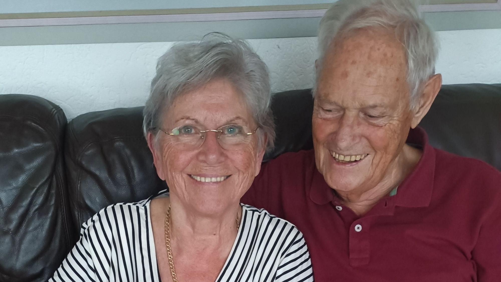 Das Foto zeigt das Ehepaar, wie es auf einem schwarzen Sofa sitzt. Ingeborg lacht in die Kamera und Peter blickt lächelnd nach unten.